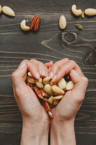 Hands holding nuts in heart shape on the wooden table. Nuts mix with seeds and dried fruits on the wooden table.